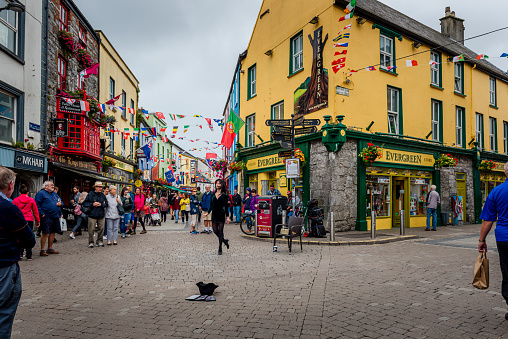 Galway, Ireland - August 07, 2018: People walking along one of the main pedestrian streets in Galway. It is full of shops, pubs and restaurants. A girl is tap-dancing.