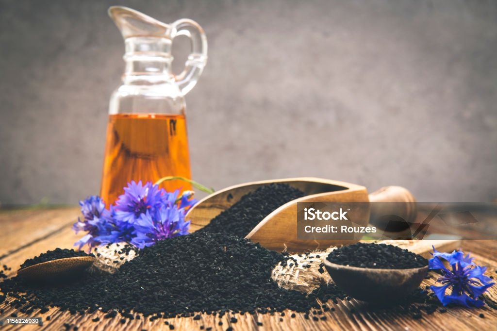 Black cumin seeds essential oil with wooden spoon and shovel on wooden background Nigella oil seeds and flower on wooden table with space Nigella Stock Photo