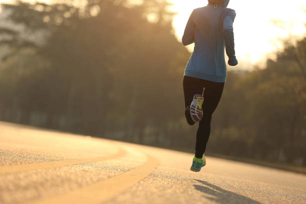 junge fitness-läuferin läuft auf sonnenaufgangsstraße - running jogging women marathon stock-fotos und bilder