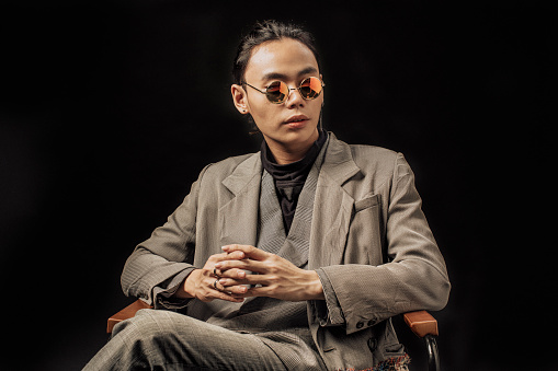 an asian chinese male studio portrait sitting on the chair with sunglasses looking away