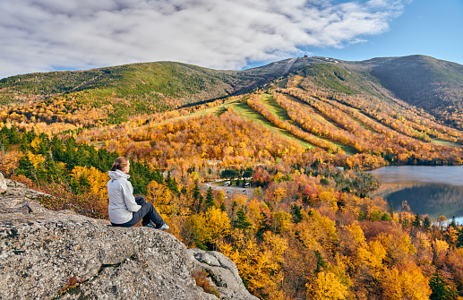 Woman hiking at Artist's Bluff in autumn. View of Echo Lake. Fall colours in Franconia Notch State Park. White Mountain National Forest, New Hampshire, USA
