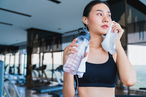 asian healthy aport woman relaxing in gym after workout hand hold pure water drink and white towel