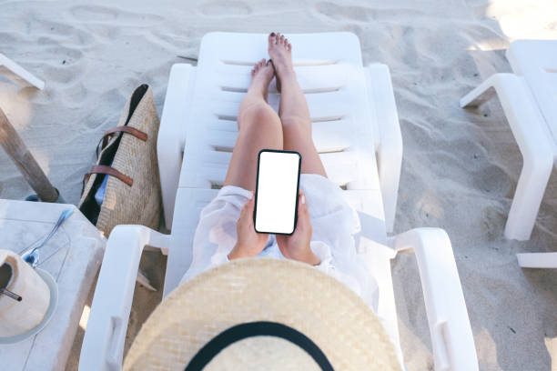 istock Top view mockup image of a woman holding white mobile phone with blank desktop screen while laying down on beach chair on the beach 1156240773