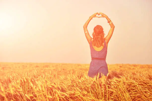Girl holding heart-shape symbol for love in a wheat field.
