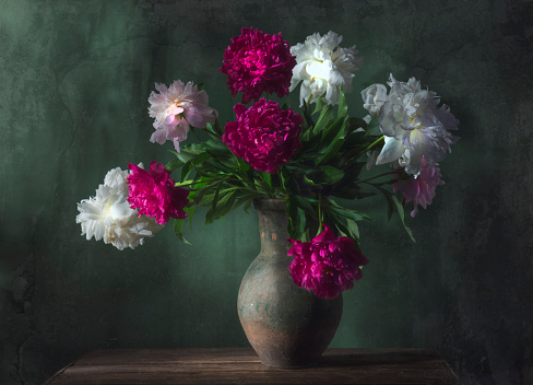 Classic still life with beautiful white and purple peony flowers bouquet in ancient jug. Art photography.
