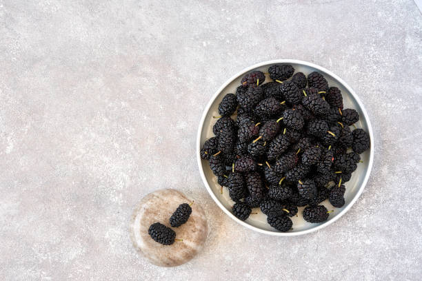 istock Fresh raw black mulberries in plate on stone background. Top view with copy space 1156245980