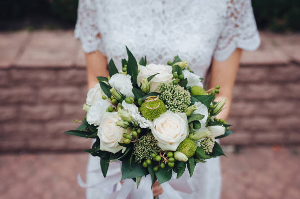 istock Wedding bouquet in bride's hands. Two gold rings lie on white roses. 1156246532