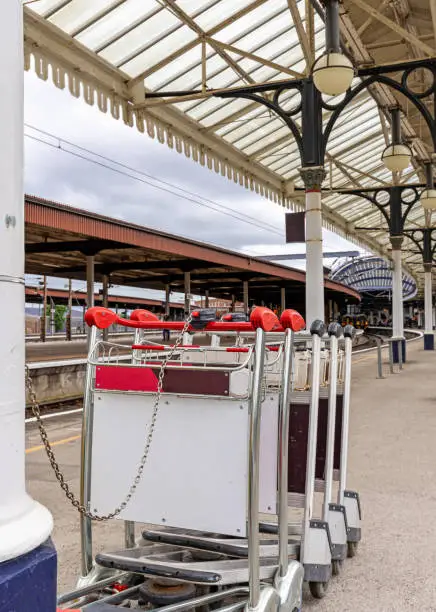 A row of luggage trolleys on a platform at York Railway Station.  A 19th Century ornate canopy is overhead.