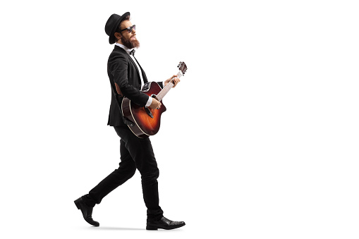 Full length profile shot of a male musician walking and playing an acoustic guitar isolated on white background