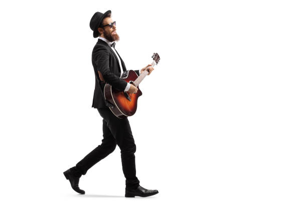 Male musician walking and playing an acoustic guitar Full length profile shot of a male musician walking and playing an acoustic guitar isolated on white background guitarist stock pictures, royalty-free photos & images