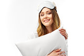 Photo shot of glad happy woman holds soft white pillow, sleeps well at night, enjoys rest, comfort and leisure, has cheerful expression. Beautiful lady model is standing at white background in Studio