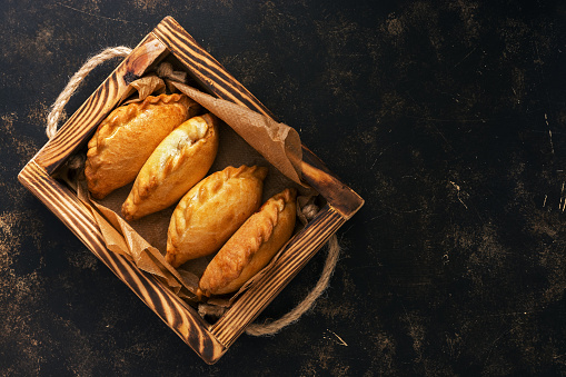 Traditional Russian pies in a wooden tray on a dark rustic background. Russian pirozhki ,baked patties. Top view, copy space, flat lay