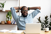 Smiling Afro-American businessman holding hands behind head sitting at office