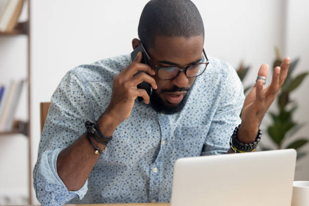 wütender verrückter afrikanisch-amerikanischer geschäftsmann spricht auf handy im büro - frustration computer confusion businessman stock-fotos und bilder