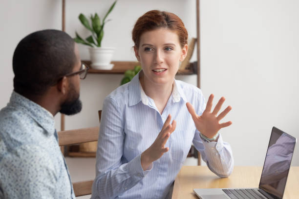 two diverse businesspeople chatting sitting behind laptop in office - discussion talking business explaining imagens e fotografias de stock