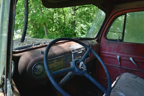 A very old, very used dump truck interior with an old dashboard and very thin steering wheel, took a real man to drive a truck in those days