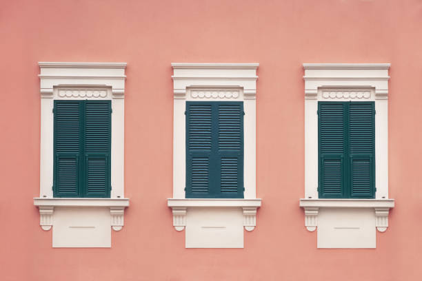three green wooden window with shutters in a white frame on pink wall