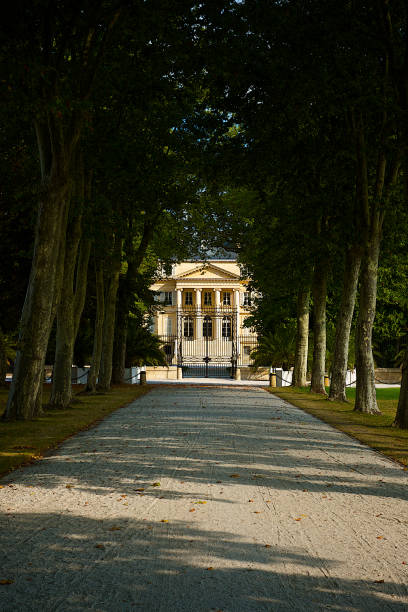 Chateau Margaux, Bordeaux region, France. Margaux, France-08 23 2013:Facade of the Château Margaux at the end of the driveway, which is a wine estate of Bordeaux wine, and was one of four wines to achieve Premier cru (first growth) status in the Bordeaux Classification of 1855.The estate is located in the commune of Margaux on the left bank of the Garonne estuary in the Médoc region, in the département of Gironde, France. tree lined driveway stock pictures, royalty-free photos & images
