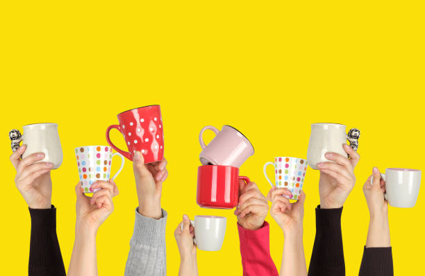 istock many raised hands up with ceramic cups on a yellow background 1156283233