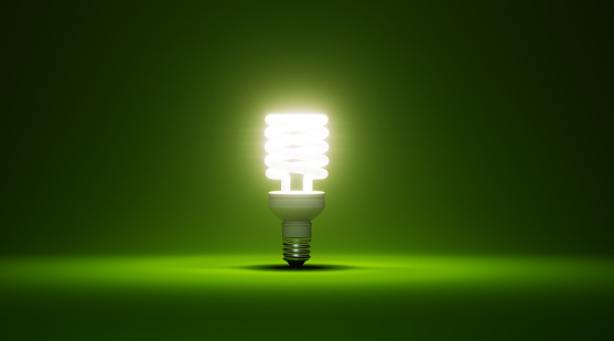 Energy saver light bulb glowing on green background. Horizontal composition with copy space.