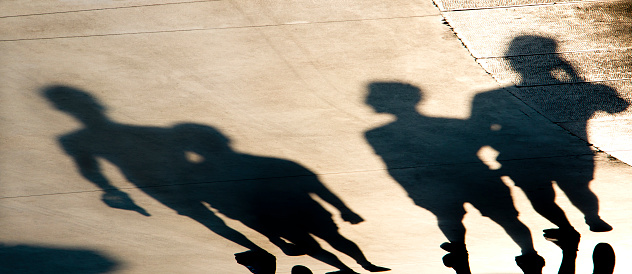 Blurry shadows silhouettes of young people walking on summer sunset promenade