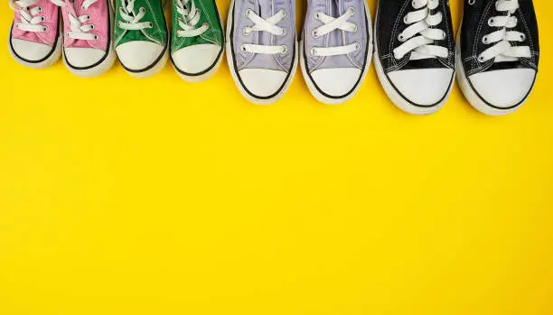 lot of textile worn sneakers of different sizes on a yellow background, empty space at the top, family concept