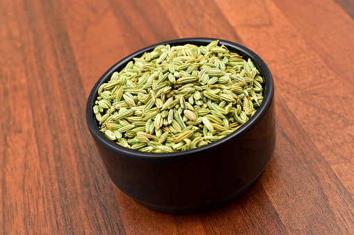 Fennel seeds in a blacl bowl on wooden table.