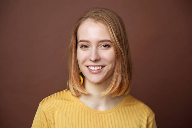 Studio portrait of an attractive 18 year old blonde woman in a yellow T-shirt on a brown background stock photo