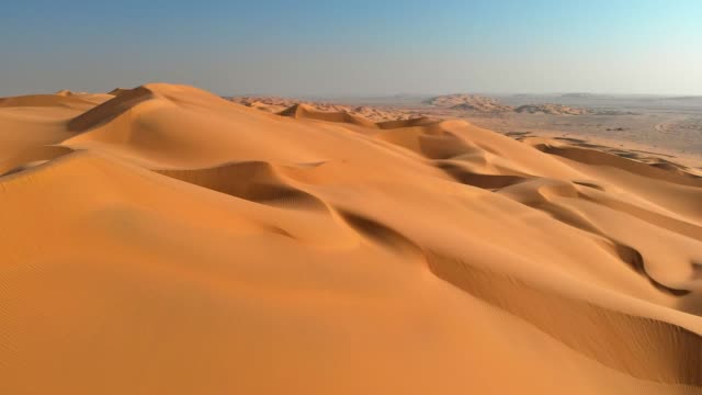 Aerial shot of sand dunes in desert. Flying over endless yellow sand dunes at sunset