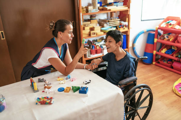 insegnante esperto che lavora con un adolescente latino con celebral palsy in sedia a rotelle. - alternative health care foto e immagini stock