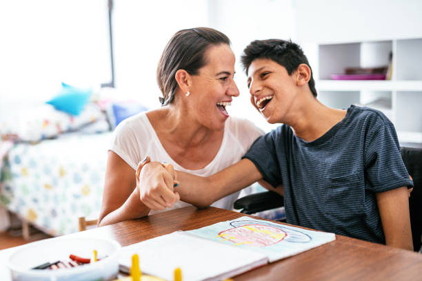 Disabled Latino teenager with Celebral Palsy and mother laughing. Cerebral palsy are lifelong conditions that affect movement and co-ordination, caused by a problem with the brain that occurs before, during or after birth. alternative lifestyle stock pictures, royalty-free photos & images