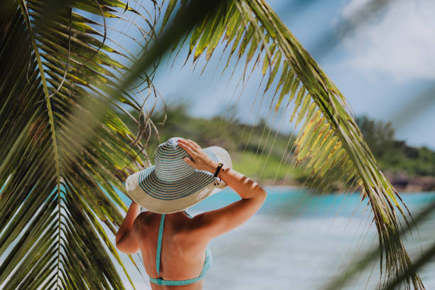 mujer en la playa en la sombra de las palmeras con sombrero azul. concepto de vacaciones recreativas para el paraíso de lujo - beach sea zen like nature fotografías e imágenes de stock