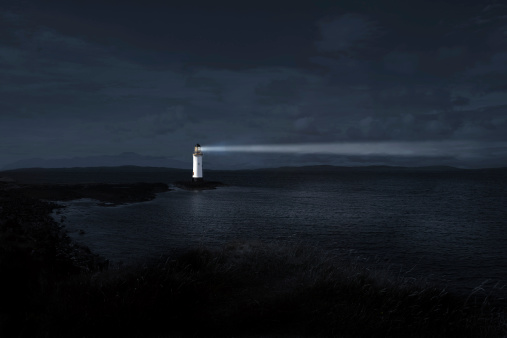 Light house at night projecting a powerful beam into the night to guide those who are lost