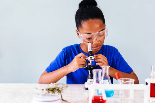 Young African American kid using microscope in lab Young African American kid using microscope and experimenting scientific lab along with chemical substance tubes and flasks in classroom - science and learning education concept microscope isolated stock pictures, royalty-free photos & images