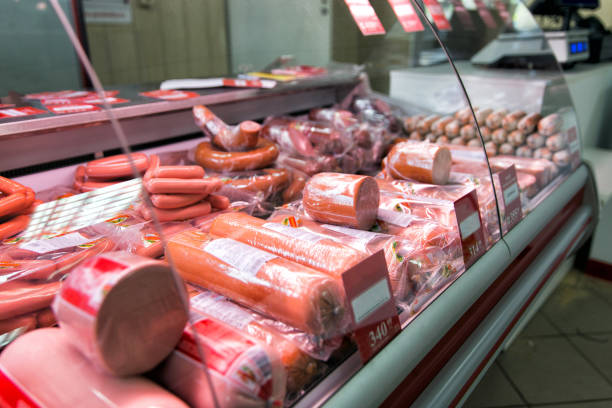 compteur avec saucisse bouillie dans le magasin. étagères de réfrigérateur avec différents produits de viande - charcuterie traiteur photos et images de collection