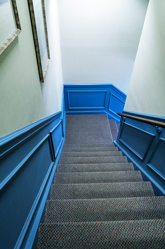 Looking down a steep carpeted staircase from the top step toward the corner landing where it turns to the right.