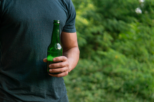 Man holding a beer bottle in nature, green background for a drink ad, copy space, empty space