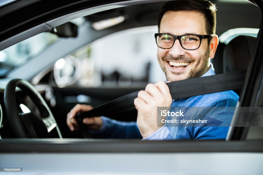 Happy businessman fastening seatbelt before his trip by car. Young happy man fastening his seatbelt before a trip by car and looking at camera. Car Stock Photo
