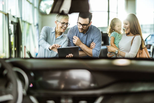 車のショールームでデジタルタブレットを使用して若い幸せな家族と女性の販売員。 - digital tablet looking child offspring ストックフォトと画像