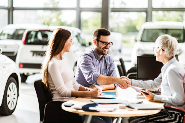 Congratulations, we have a deal about buying a car! Happy couple came to an agreement with car salesperson on a meeting in a showroom. Focus is on man. car ownership photos stock pictures, royalty-free photos & images