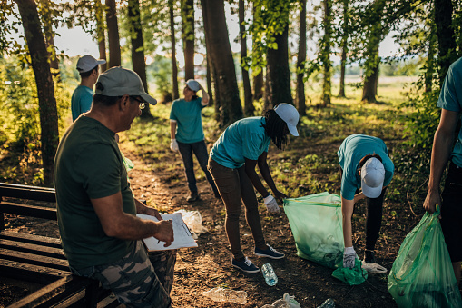 Group of volunteers with blue t-shirts, caps and protective gloves picking up garbage in a park.