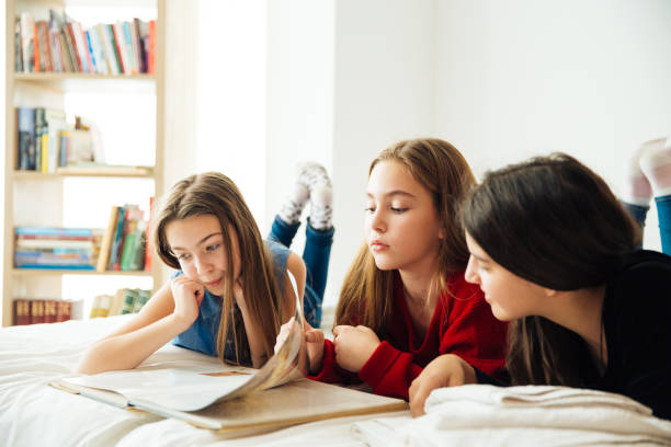 istock Three Happy Sisters Lying in Bedroom and Reading a Book. 1156328635