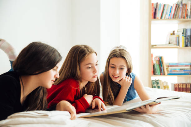 istock Three Happy Sisters Lying in Bedroom and Reading a Book. 1156328644