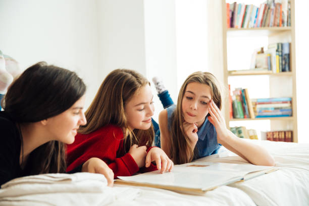 istock Three Happy Sisters Lying in Bedroom and Reading a Book. 1156328664