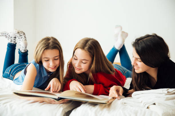 istock Three Happy Sisters Lying in Bedroom and Reading a Book. 1156328671