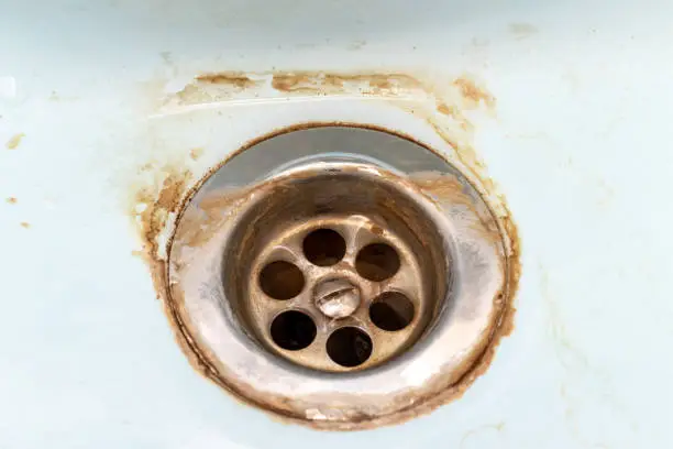 Photo of Dirty sink drain mesh, hole with limescale or lime scale and rust on it close up, dirty rusty bathroom washbowl
