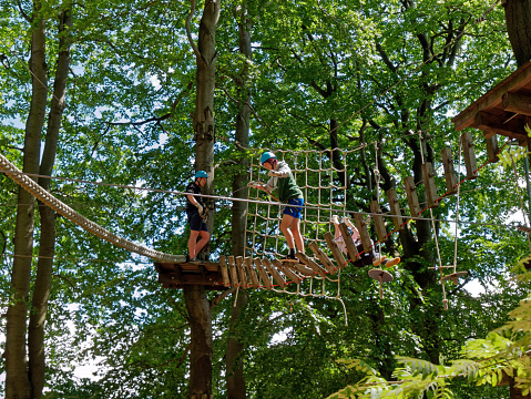 Hoherodskopf, Germany - June 15, 2014: Visitors in a climbing forest / Hochseilgarten / Klettergarten in Germany. Some people climbing, jumping or balancing. Other watching the climber between the trees.