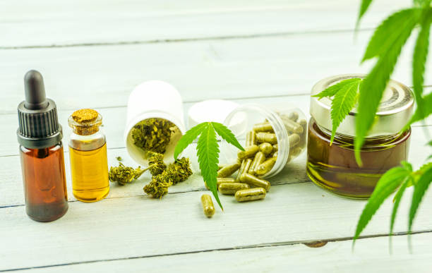 bottiglie di vetro all'olio di cannabidiolo cbd, boccioli di fiori di pillole e foglie di cannabis su uno sfondo di legno luminoso - anticancer foto e immagini stock