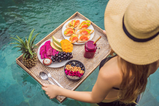 breakfast tray in swimming pool, floating breakfast in luxury hotel. girl relaxing in the pool drinking smoothies and eating fruit plate, smoothie bowl by the hotel pool. exotic summer diet. tropical beach lifestyle. bali trend - flutuar na agua imagens e fotografias de stock