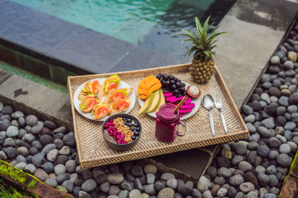 istock Breakfast on a tray with fruit, buns, avocado sandwiches, smoothie bowl by the pool. Summer healthy diet, vegan breakfast. Tasty vacation concept 1156355382